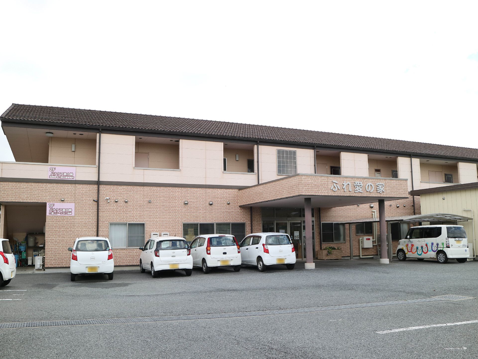 2階建ての施設外観と、複数台の車を停めることができる広い駐車場