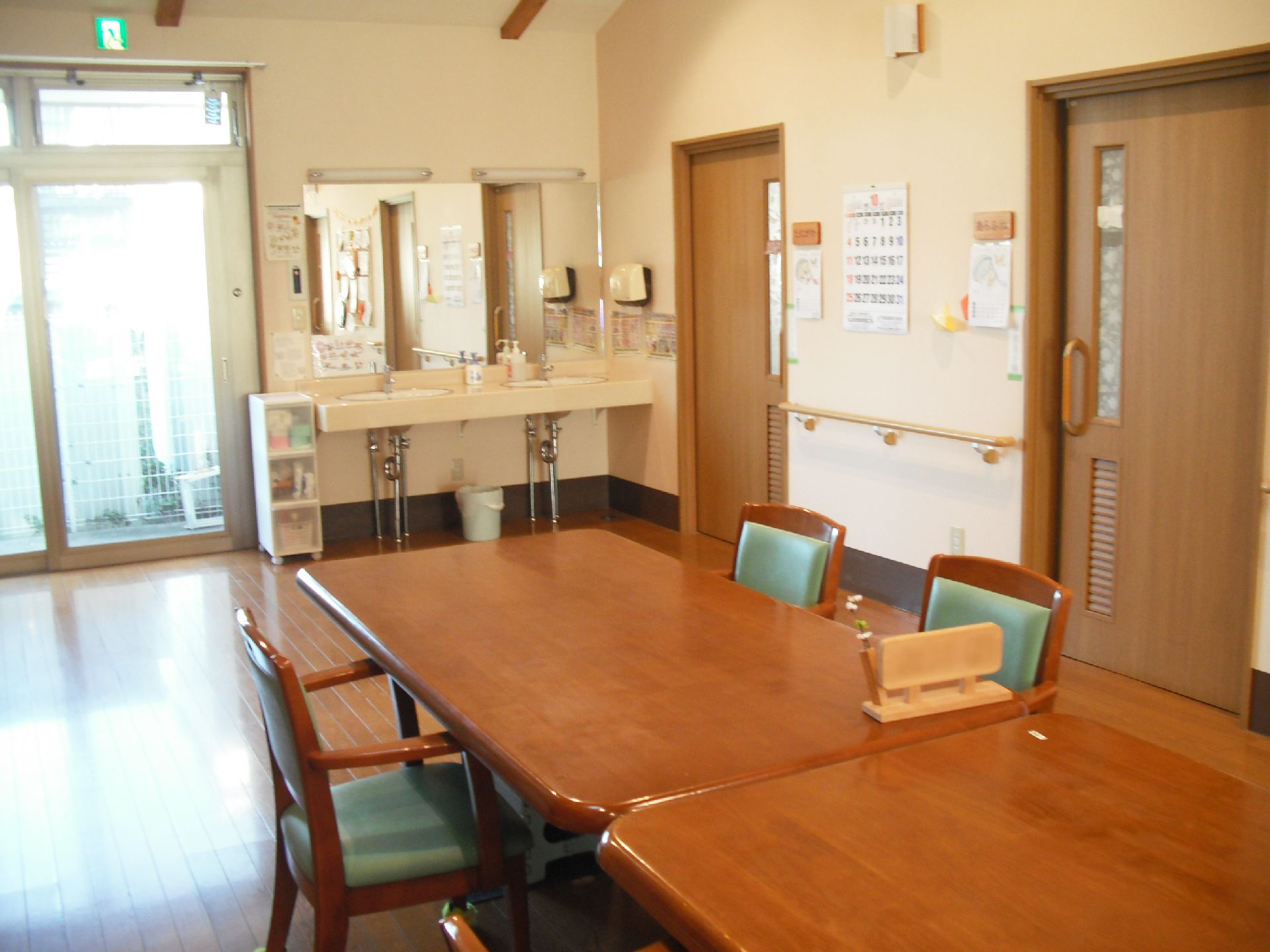 グレーの三角屋根が付いた平屋建ての建物。建物の玄関からは手すり付きのスロープが続き、駐車場もある。