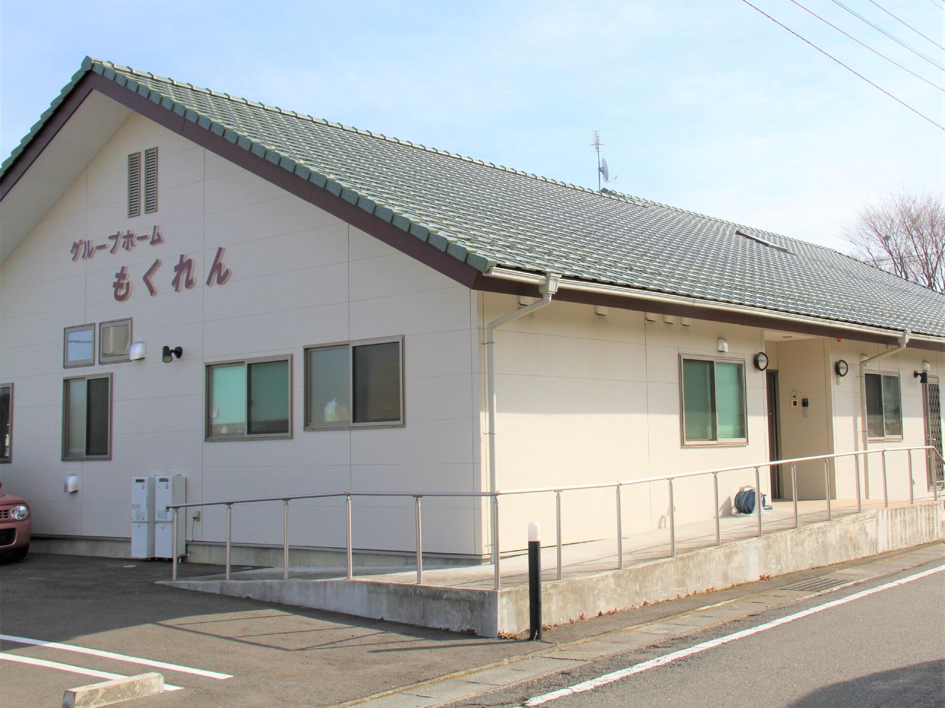 エアコンが付いたシンプルな居室には寝具付きのベッドやテレビ、タンスがあり、壁には作品が飾られている。大きな窓にはカーテンもついている。