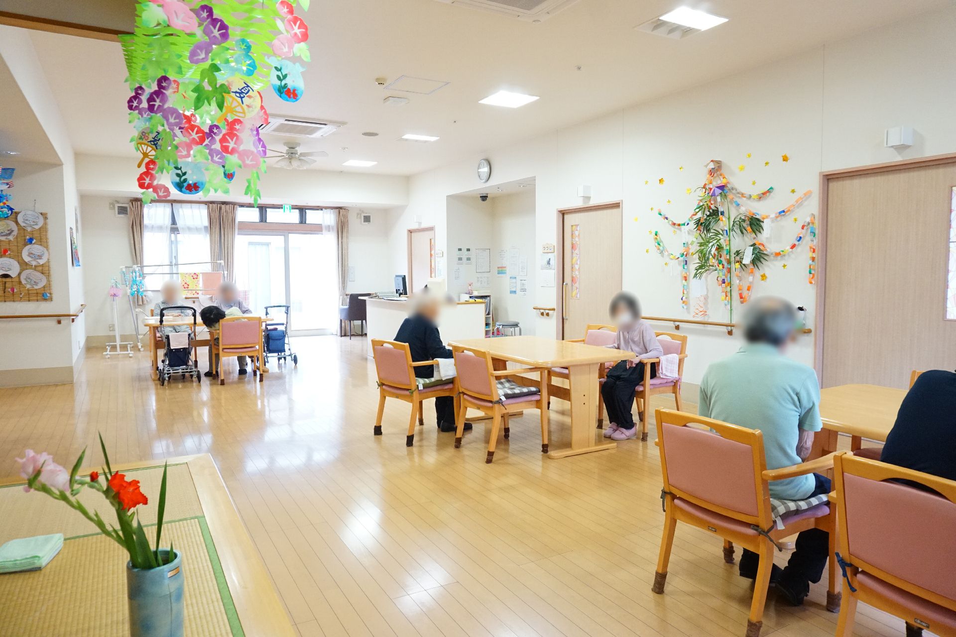 窓から陽光が降り注ぎ、テーブル、椅子が多数置かれているリビング