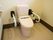 掃除の行き届いたきれいなトイレである。便器の両側には大きな手すりが設置されていて、後ろの壁にはコンセントがある。