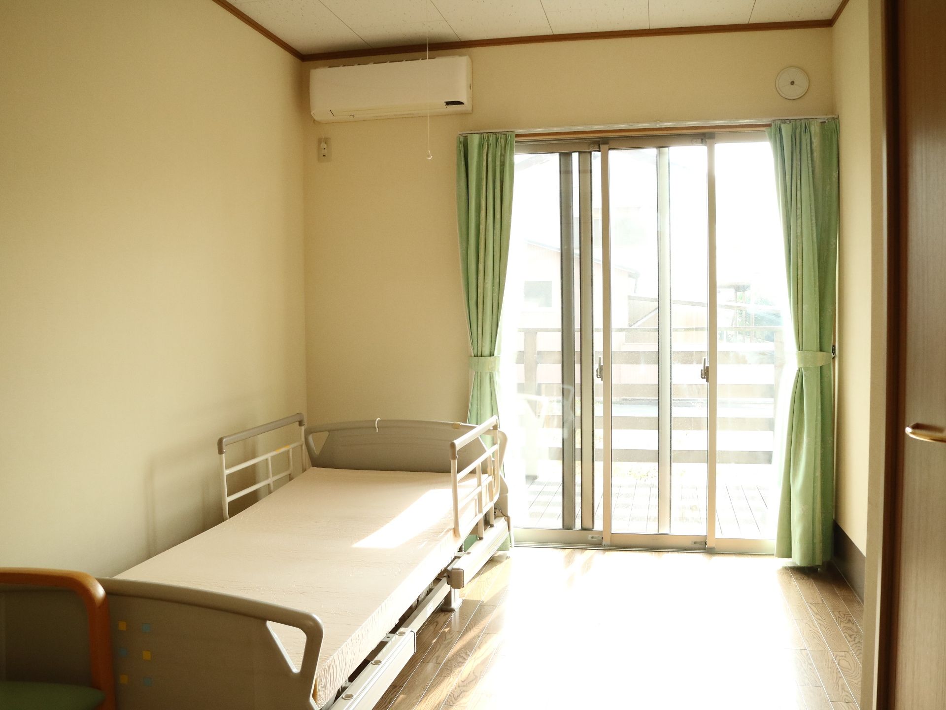 緑色のカーテンが印象的な、介護用ベッドが置かれた居室