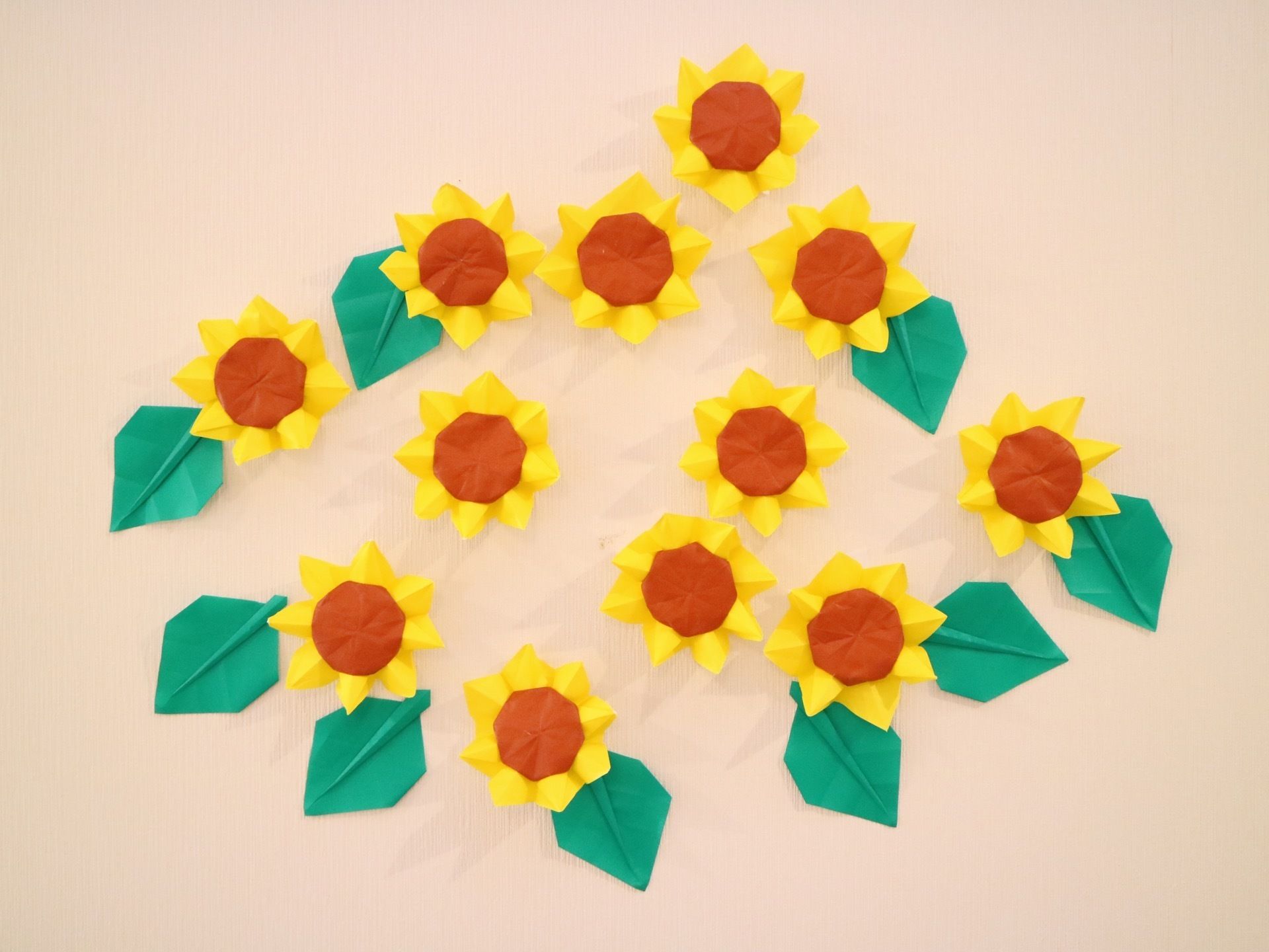 白い壁に折り紙で作られたひまわりの花が飾られている。温かみのある作品で、アットホームな雰囲気が伝わる。