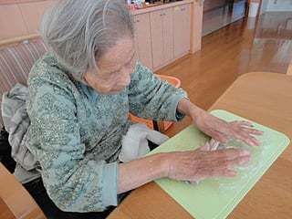 椅子に座ってお菓子を作っている高齢女性の様子。施設内のレクリエーションの一場面