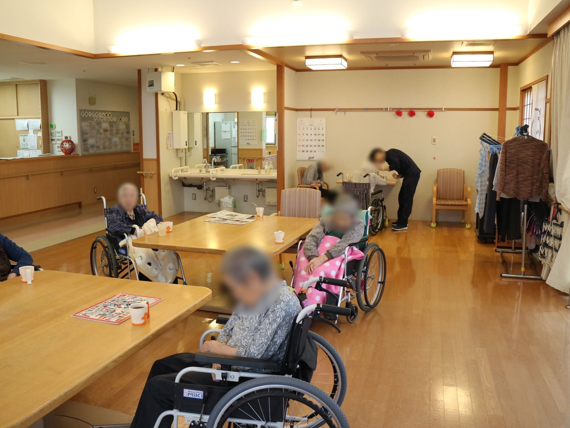食堂には幅の広いダイニングテーブルが設置されている。テーブルにはマグカップが置かれており、入居者様が席に着いている。
