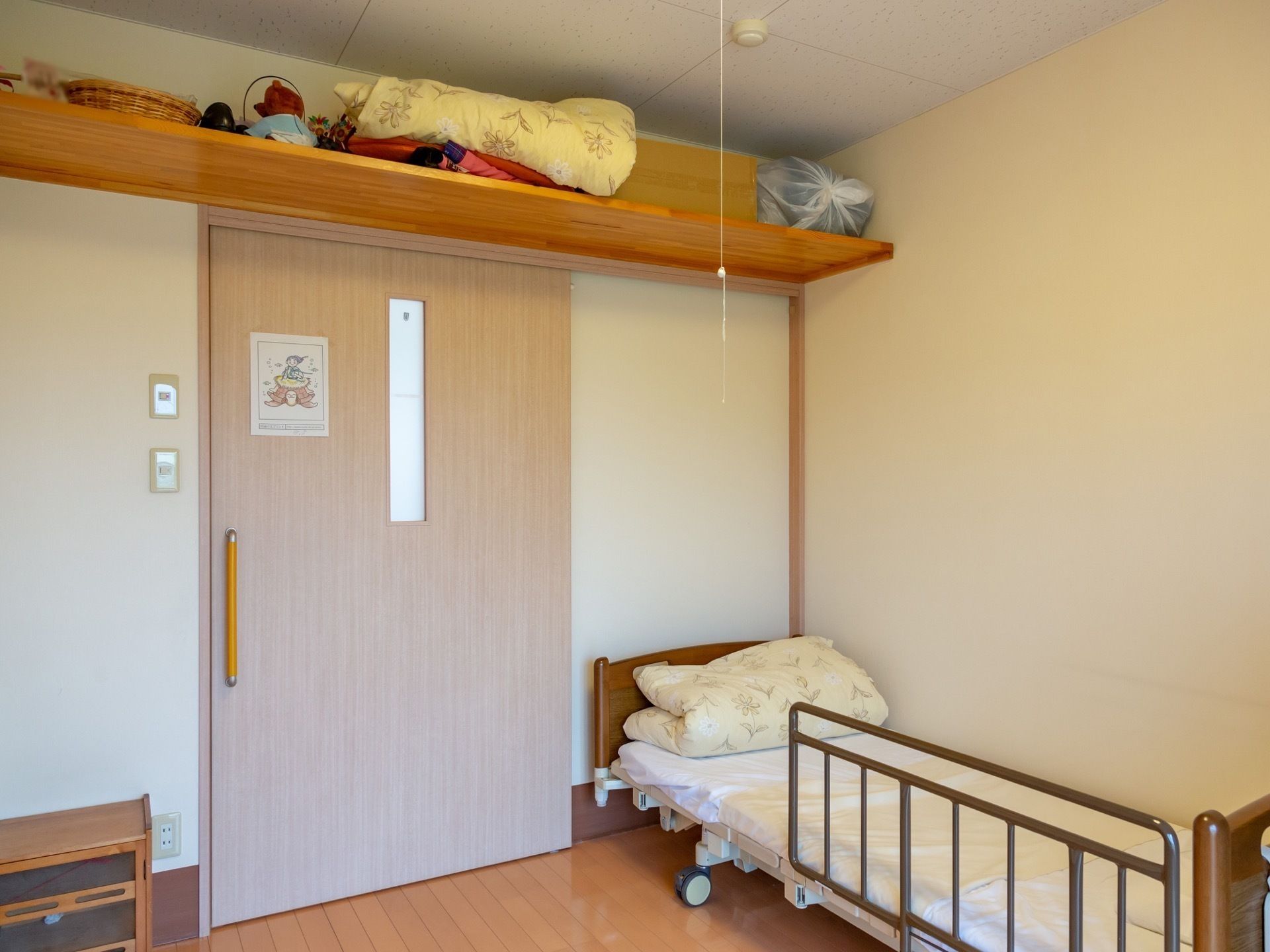 居室には、壁際に安全ガード付のベッドが置いてある。出入口の扉は引き戸になっており、扉の上部には板を渡した収納スペースが設けられている。