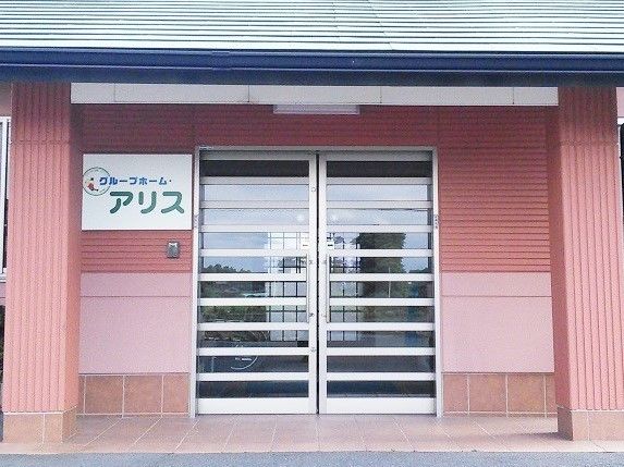 平屋建ての建物で、玄関の扉はガラス製。扉の左横にホームの表札がある。
