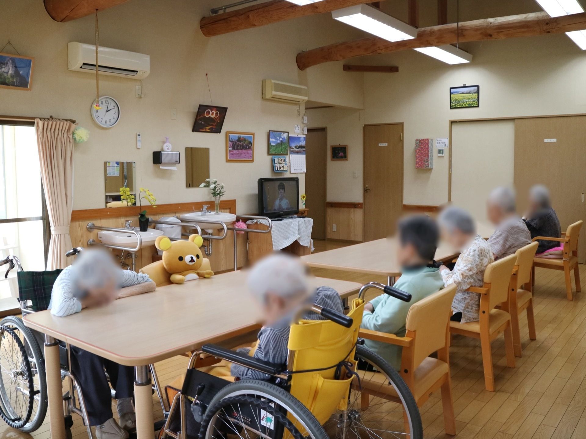 天井に梁が渡った共有スペースで、エアコンが２か所に取り付けられている。中央にあるテーブルセットで、入居者様がテレビ鑑賞などを楽しんでいる。