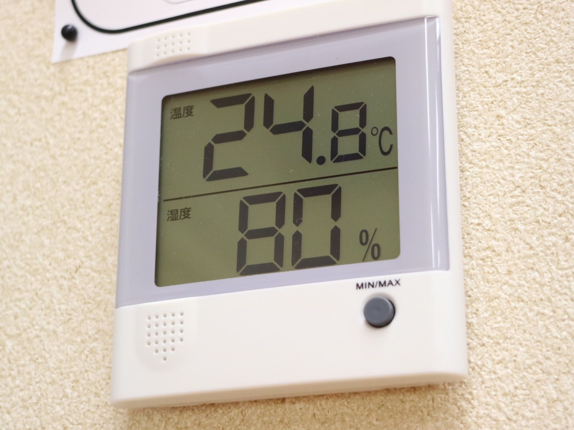 白い壁にデジタル式の温度計がかかっている。２段に分かれて表示されており、上段は気温、下段は湿度になっている。