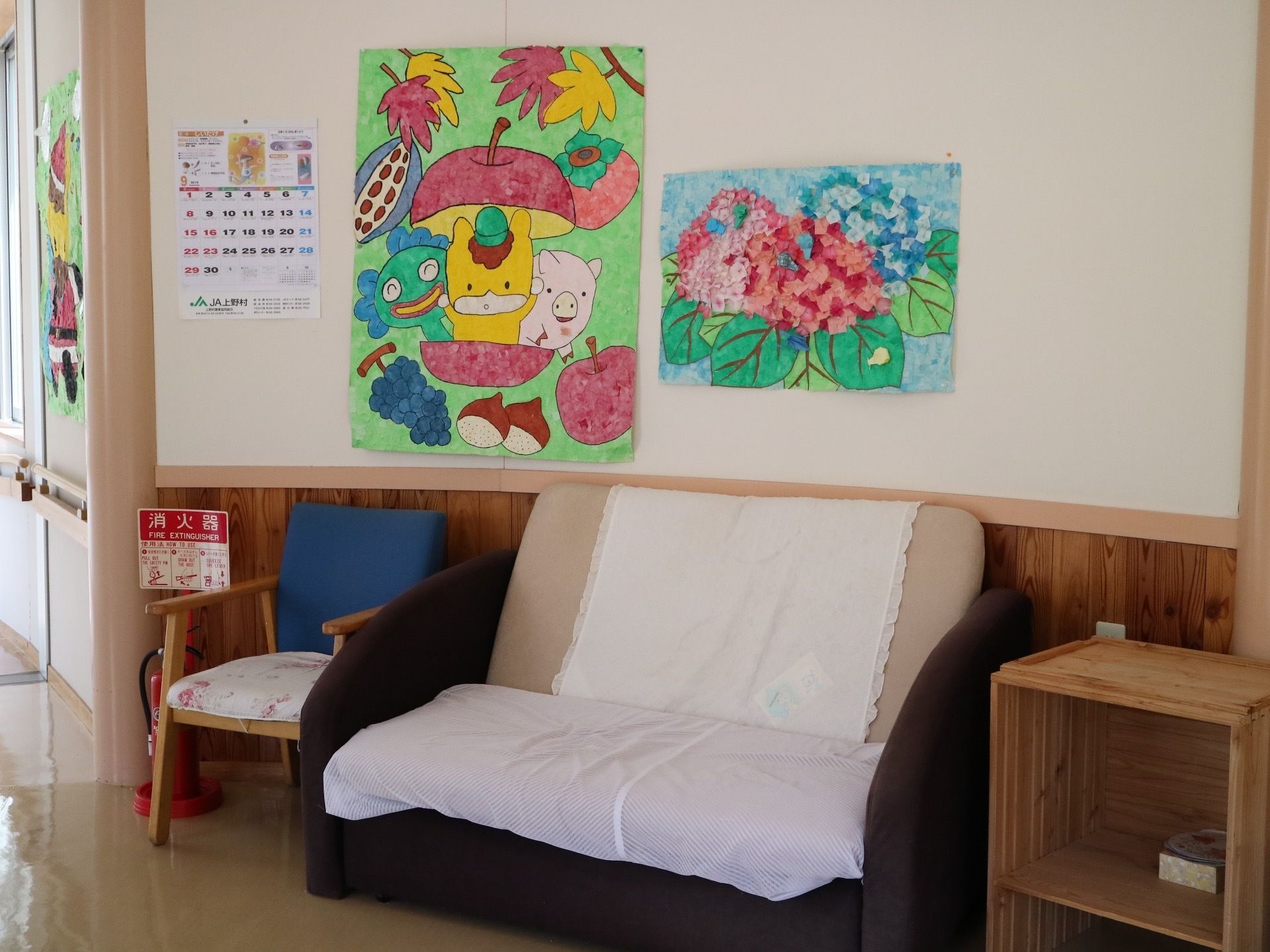 廊下の壁に沿って２人掛けのソファや椅子が並べられている。壁にはご当地キャラなどが描かれた紙が貼られている。