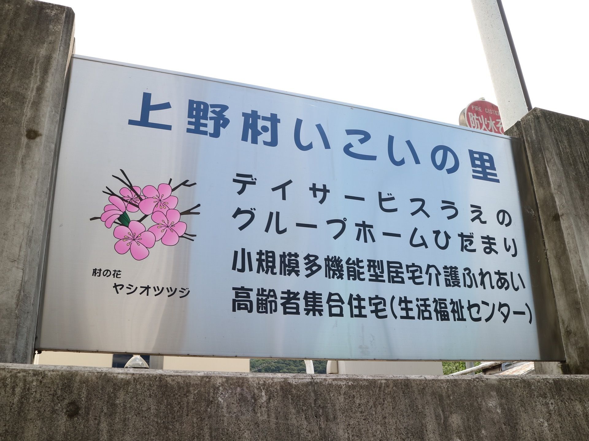 施設の外にはグループホーム敷地全体にある設備が書かれた看板がある。市町村の花のイラストなどが描かれている。