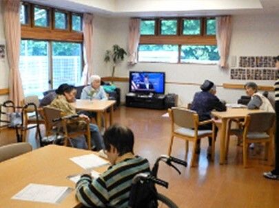 大きな窓がある明るい雰囲気の共有スペース。ダイニングテーブルセットが複数あり、テレビも設置されている。