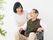 車いすに乗った男性とその人に話しかけている女性。家族で話している様子を写した写真