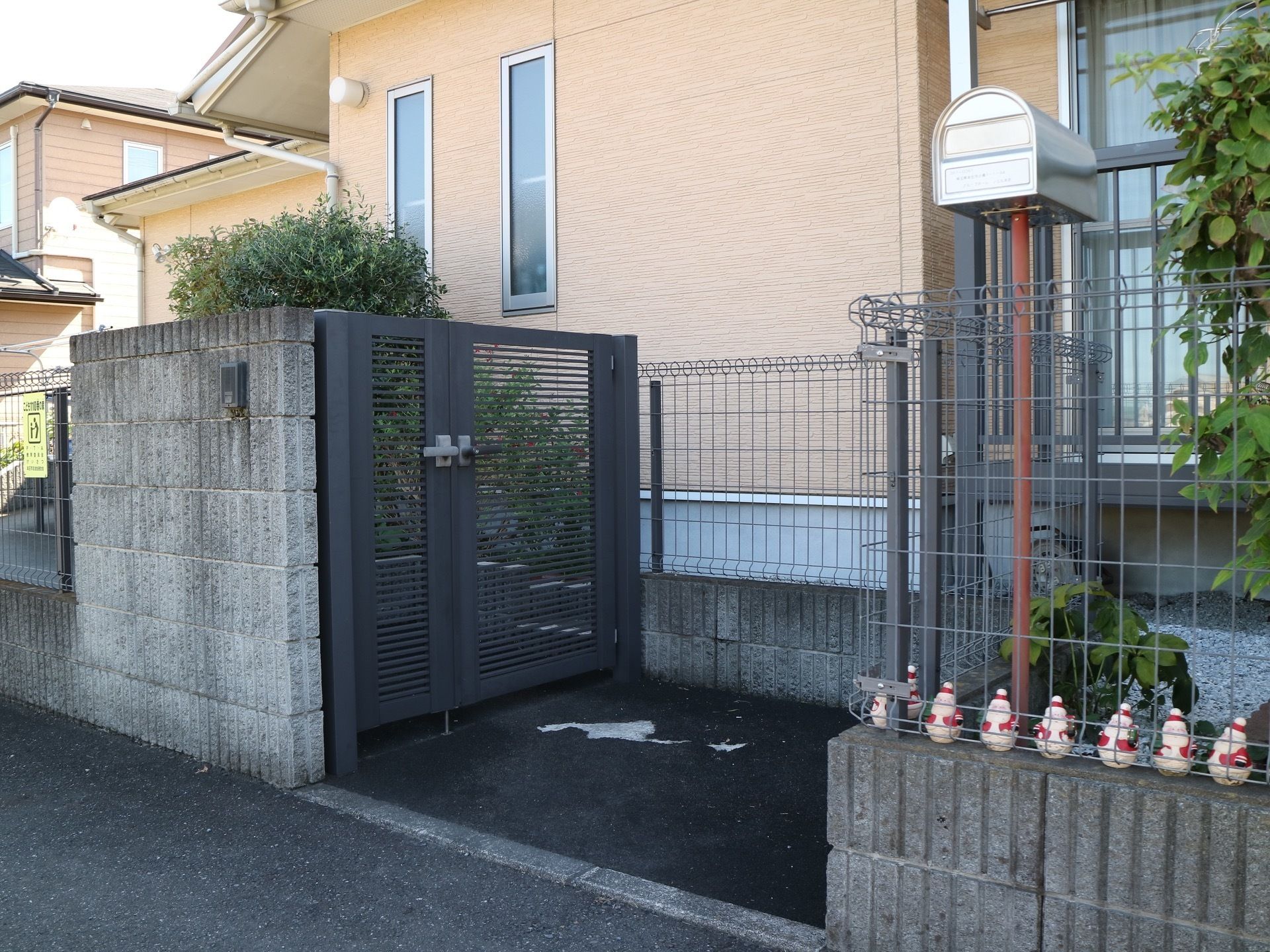 フェンスに囲まれた入り口で、ポストが立っている。フェンスの向こうには薄いオレンジ色の施設が建っている。