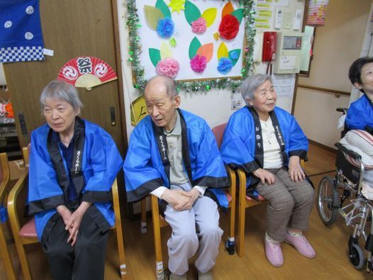 ハッピを着た入居者たちがいすに座って何かを見ている様子。館内にはお祭りに合わせた飾りつけがされている。