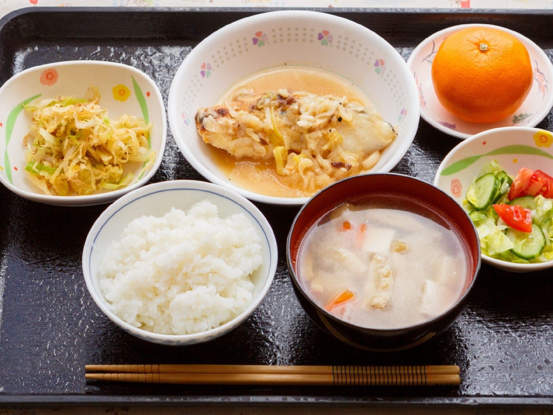 ミカンを添えた食事。魚の野菜クリーム煮や野菜の煮物、汁物、白いご飯などが並んでいる。