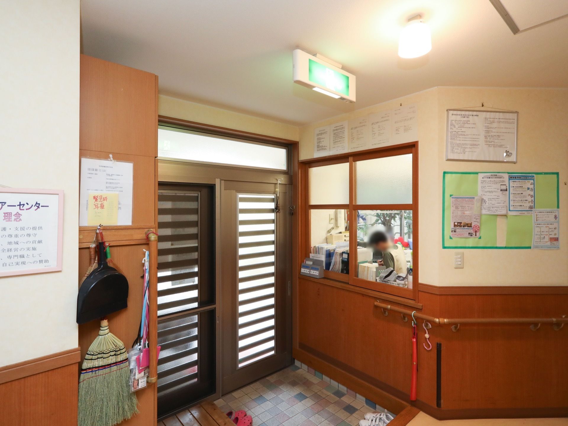 入口の扉はアルミのスライド式で、玄関に行くまでの通路には手すりが設置されている。ガラス窓から事務室の中が見える。