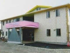 ホーム外観。２階建ての淡いベージュの建物に黄色の屋根。玄関周辺に段差はなく、玄関には屋根が付いている。