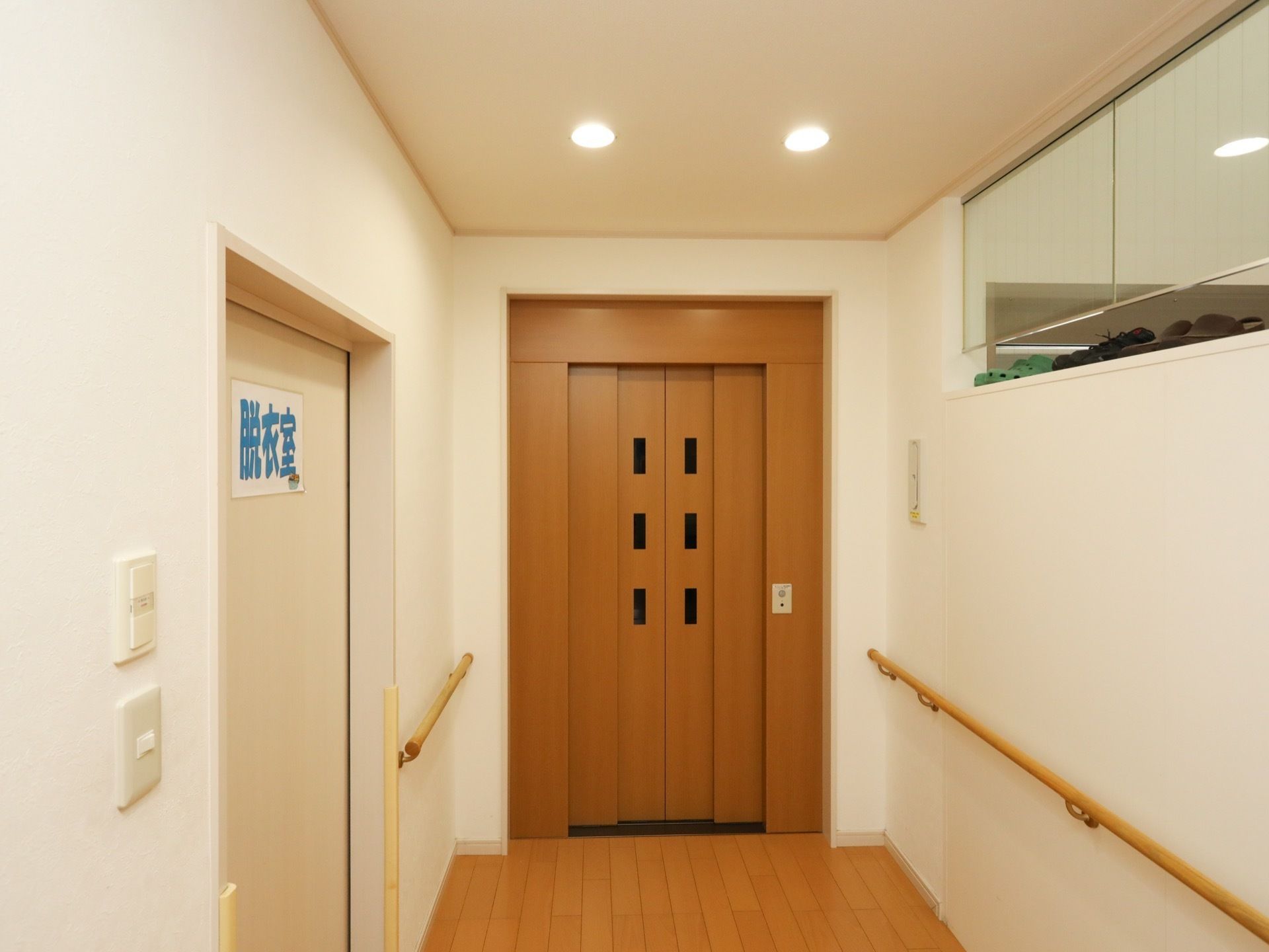 施設内にはエレベーターが設置されている。ドアはベージュ色で、エレベーターまでの壁には長い手すりが付いている。
