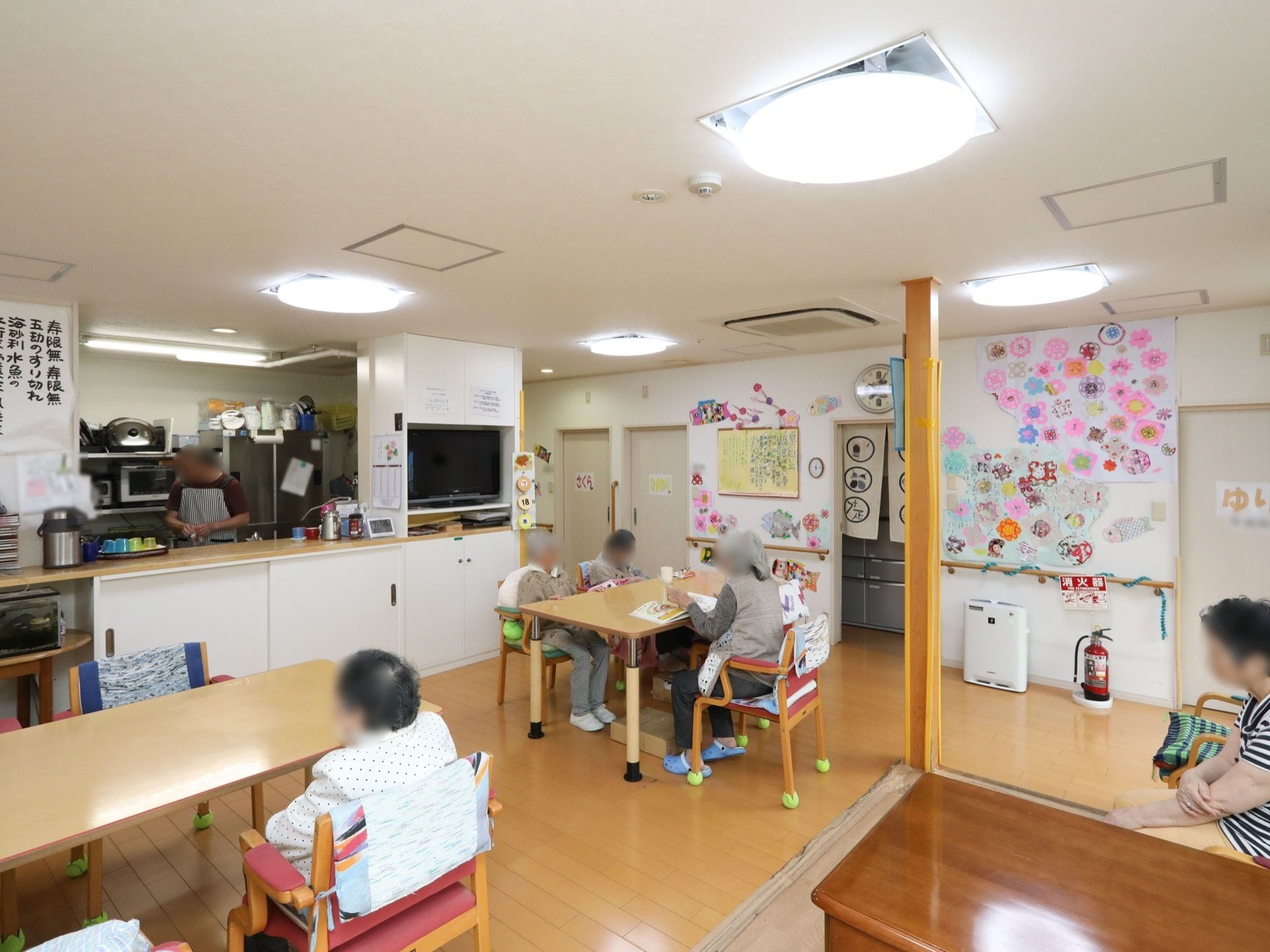 共有スペースにはテーブルが置かれ、座って本を読んでいる入居者様もいる。対面式のキッチンが付いている。
