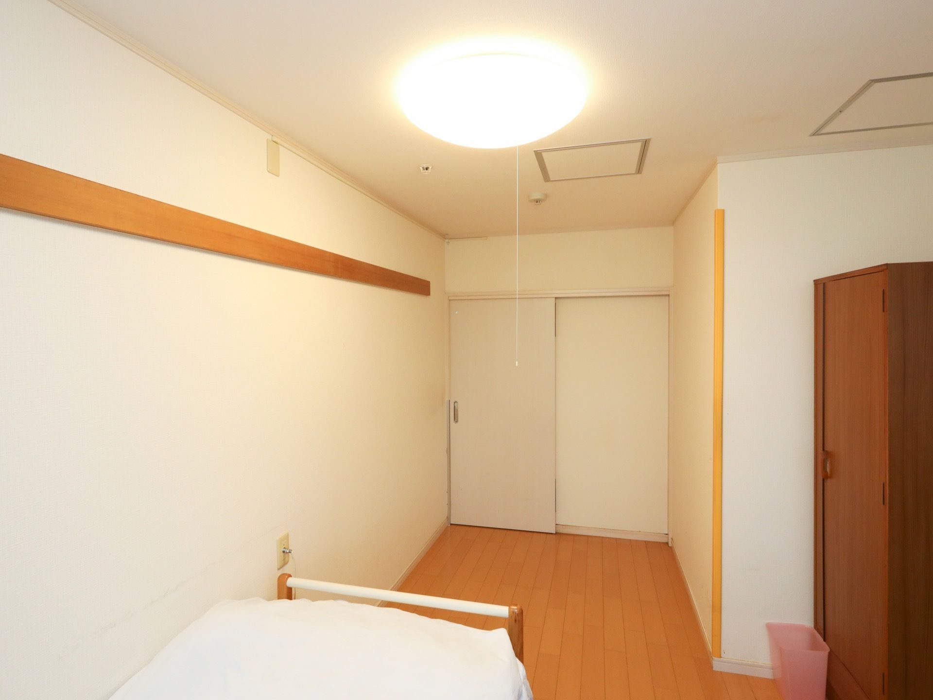 居室のドアは白色で、引き戸タイプとなっている。居室にはベッドがあり、茶色い大きなクローゼットとピンク色のゴミ箱も置いてある。