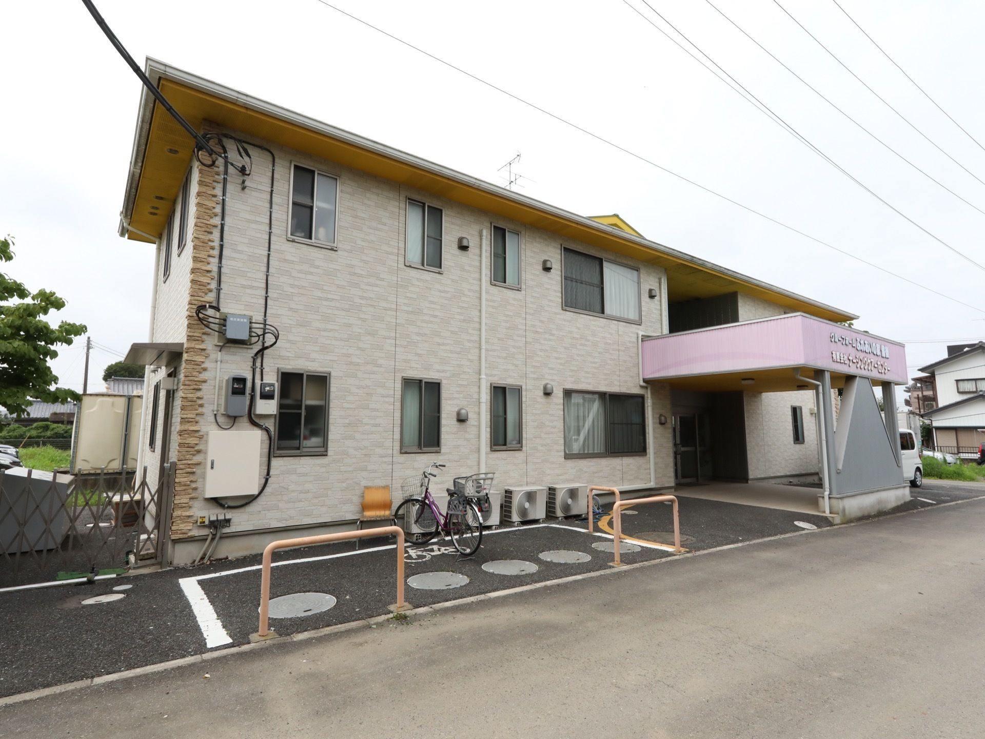 施設は２階建ての建物で、１階に入口が設置されている。ピンク色の屋根が付いている。施設前には自転車置場がある。