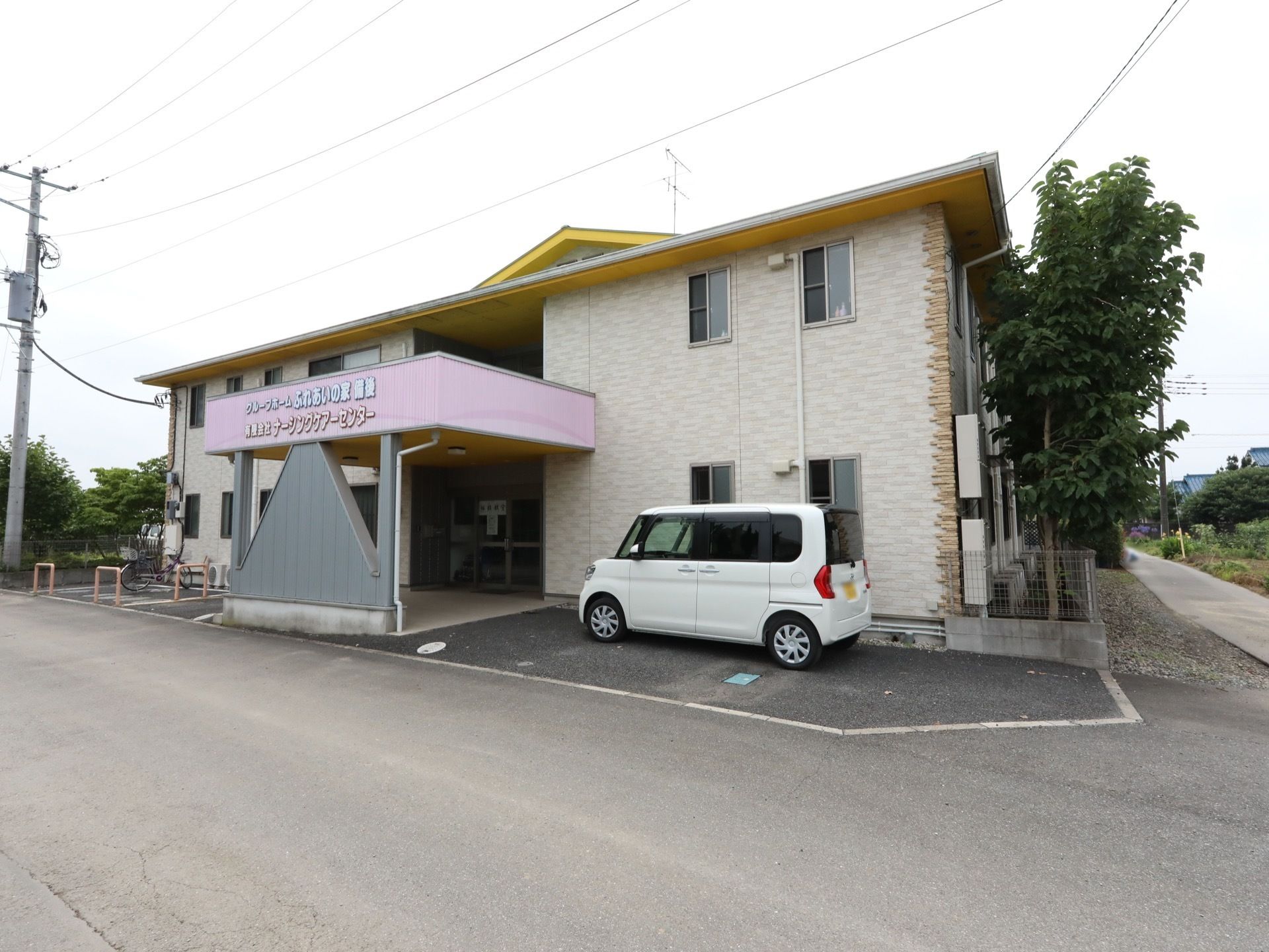 施設は横に長い２階建ての建物である。施設の前には駐車スペースがある。１階入口の屋根の部分には施設名が印字されている。