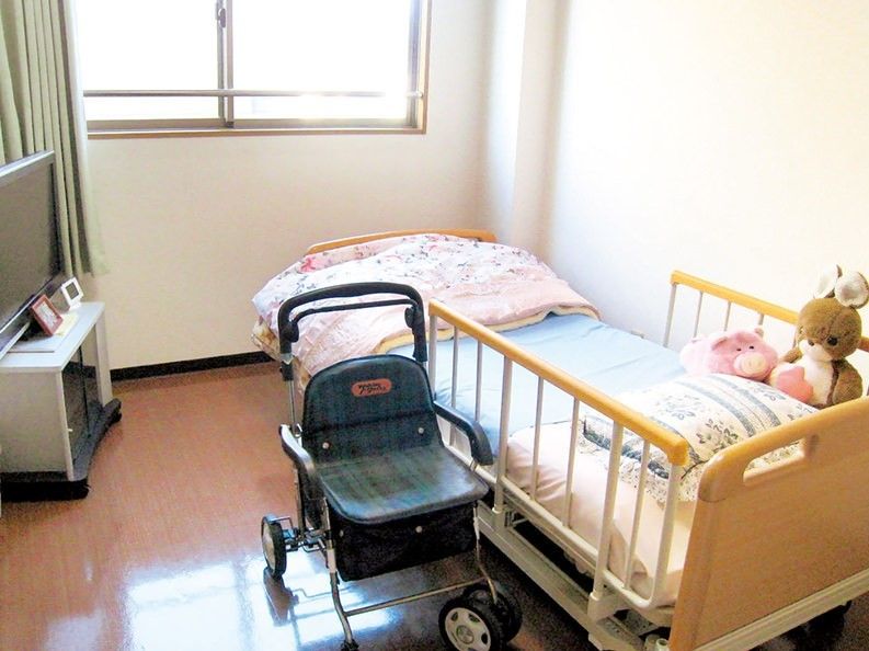 車いすとテレビが置いてある部屋。ベッドと窓、バリアフリーの床