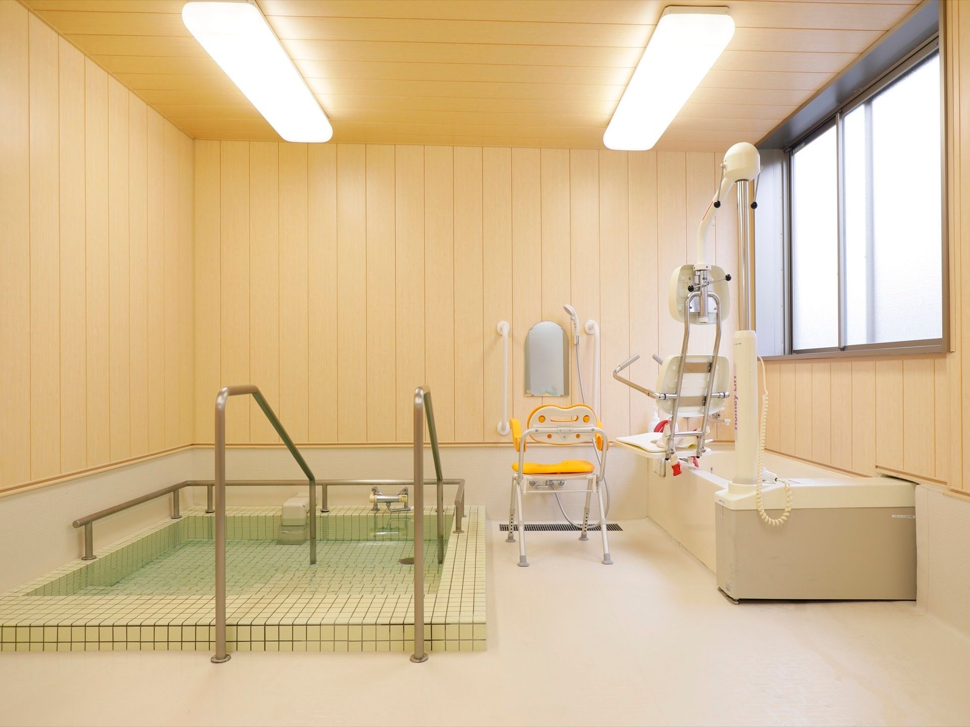 窓のある明るく広々とした浴室である。広い洗い場にはひじ掛けと背もたれのついたシャワーチェアが置かれている。
