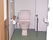 ピンクの便座が付いたトイレの壁にはトイレットペーパーホルダーと手すりがある。