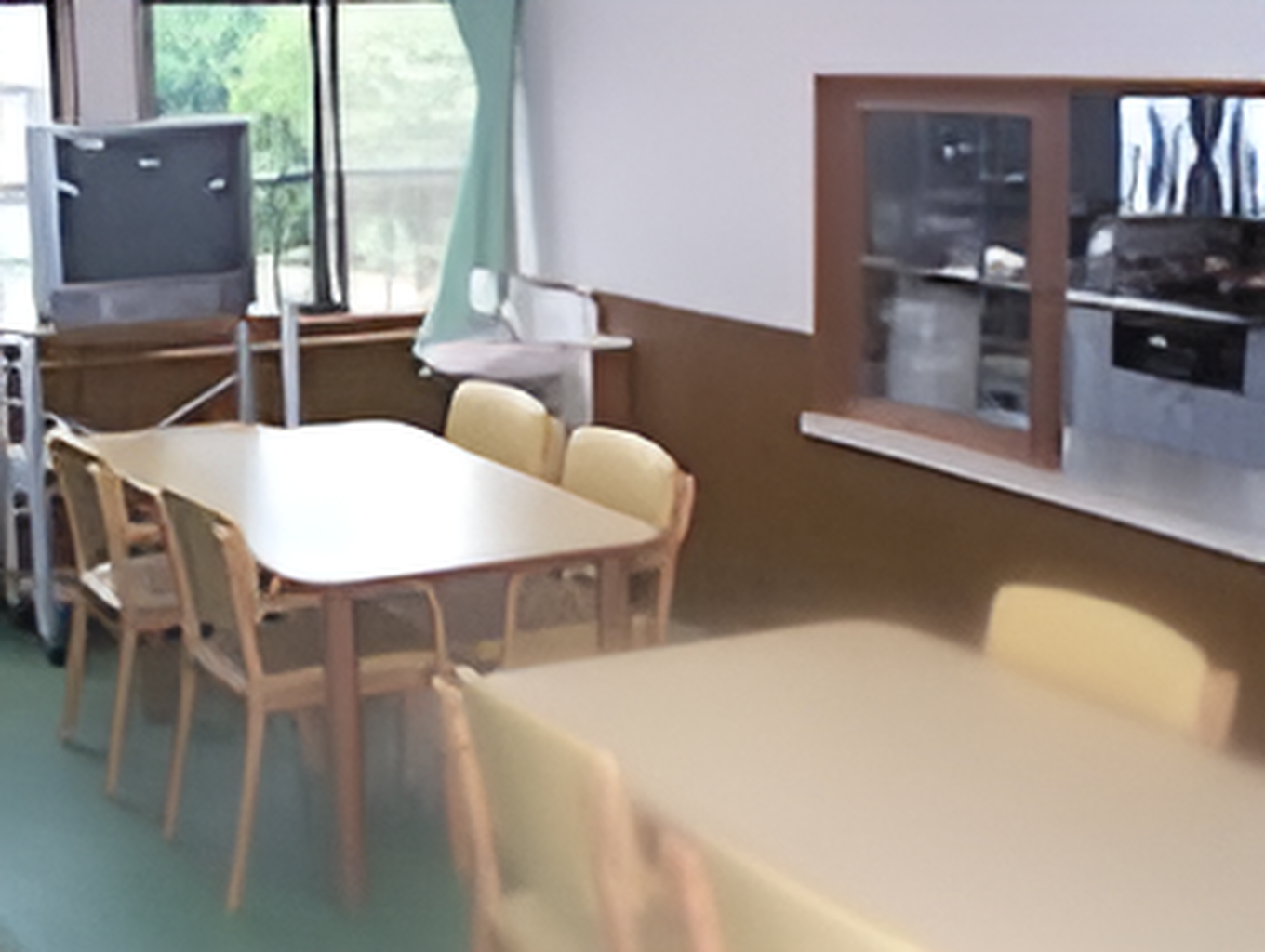 木製のテーブルセットが複数置かれた食堂にはテレビが置かれ、大きな窓にはカーテンが付いている。
