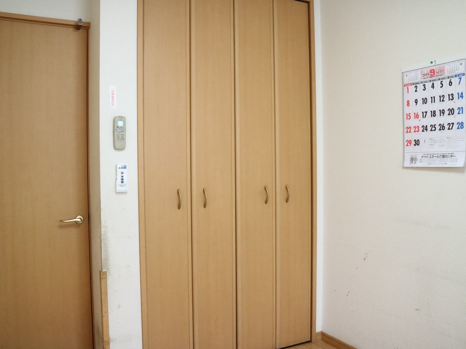 居室の一例である。中央に収納スペースがあり、両側に折れ戸が開くようになっている。右手の壁にカレンダーがぶら下がっている。