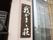 玄関横の壁に、白い文字で施設名が書かれた看板が掛けられている。その横に窓があり、すだれが下がっている。