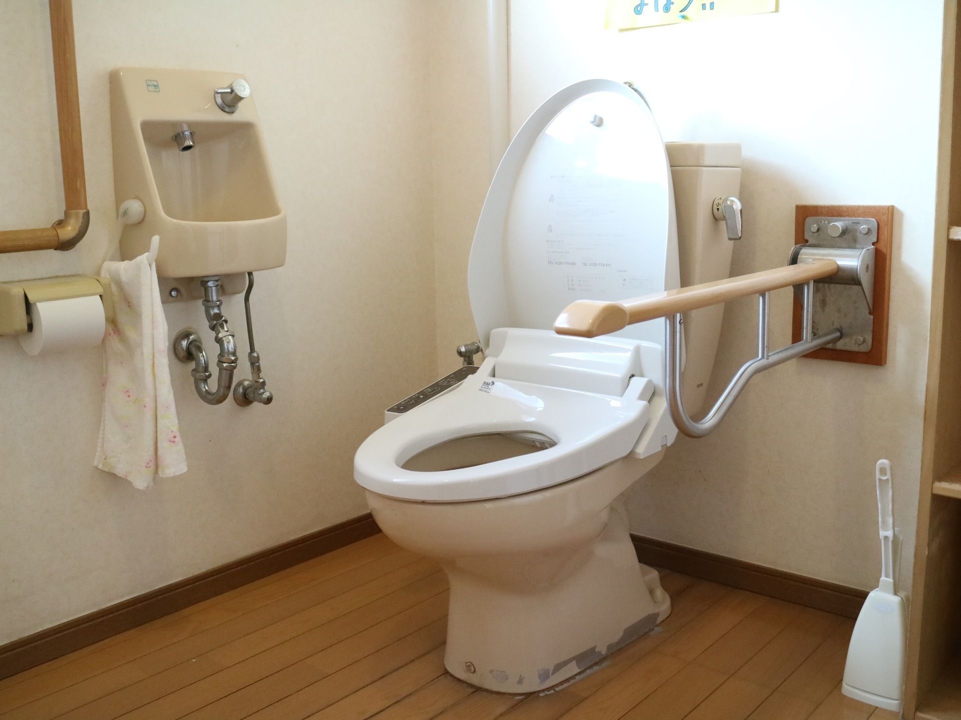 トイレの床はフローリングになっていて、温水洗浄便座が設置されている。便座の横には可動式の手すりが取り付けられている。