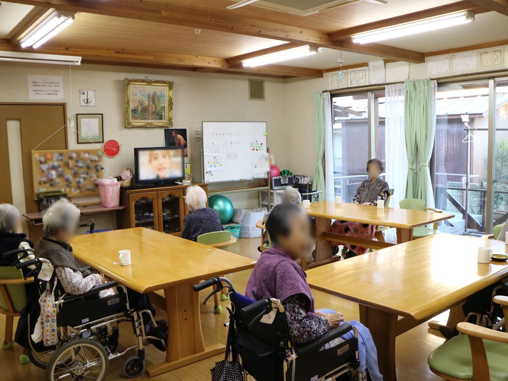 コの字型に配置されたテーブルがある、テレビの置かれた食堂に集う人々