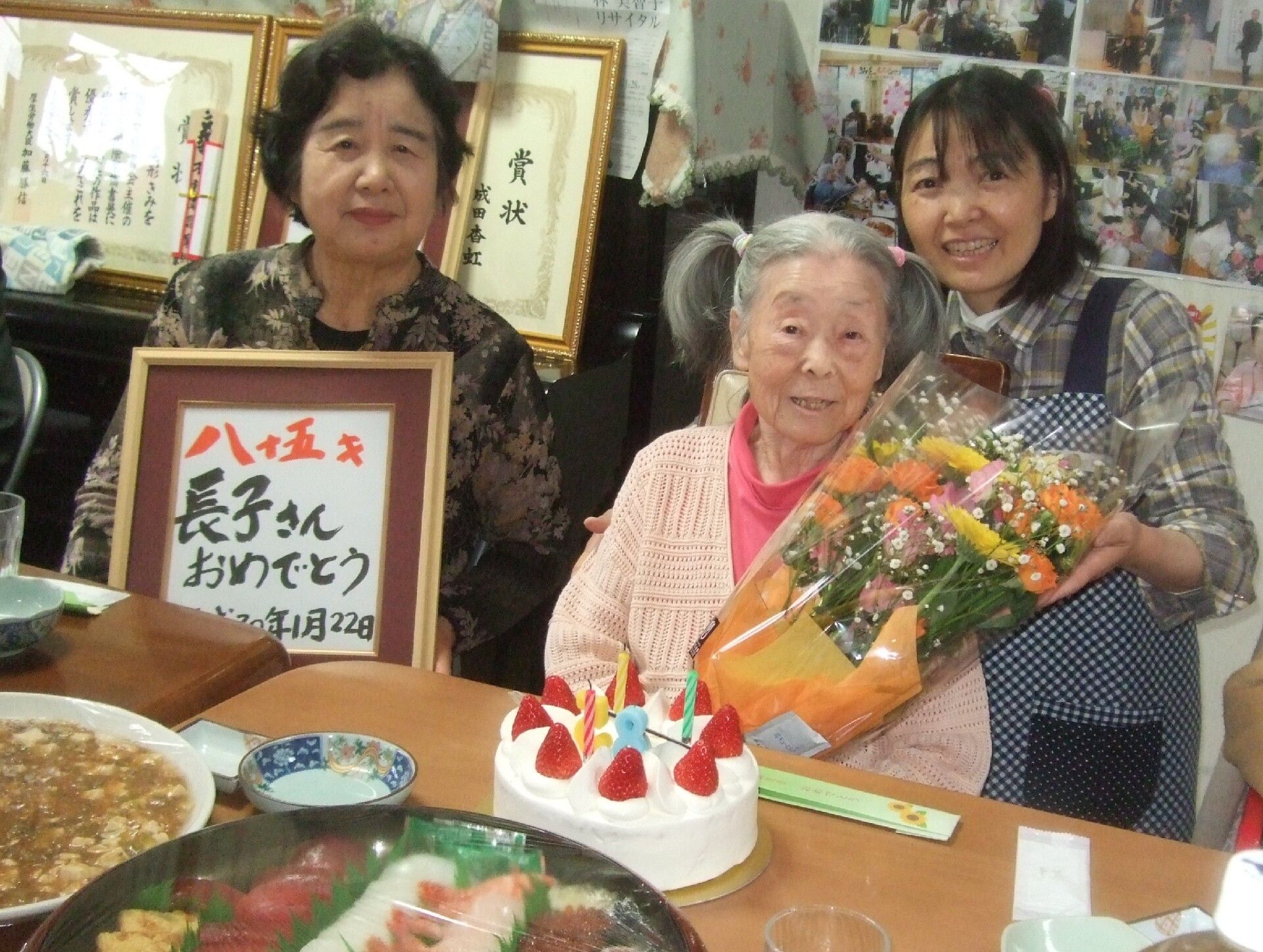 こちらを向いて笑顔になる車いすの高齢女性と介護施設の女性スタッフの様子