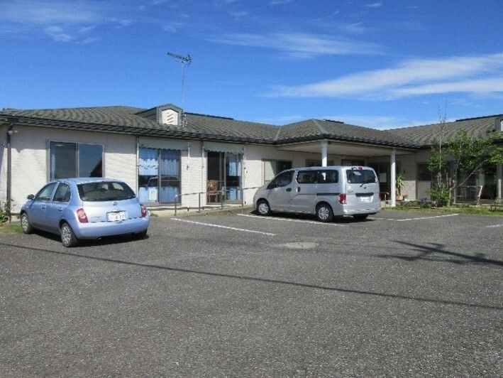 平屋建ての建物の前には駐車場があり、車が止まっている。草木が植えられた庭がありアットホームな雰囲気。