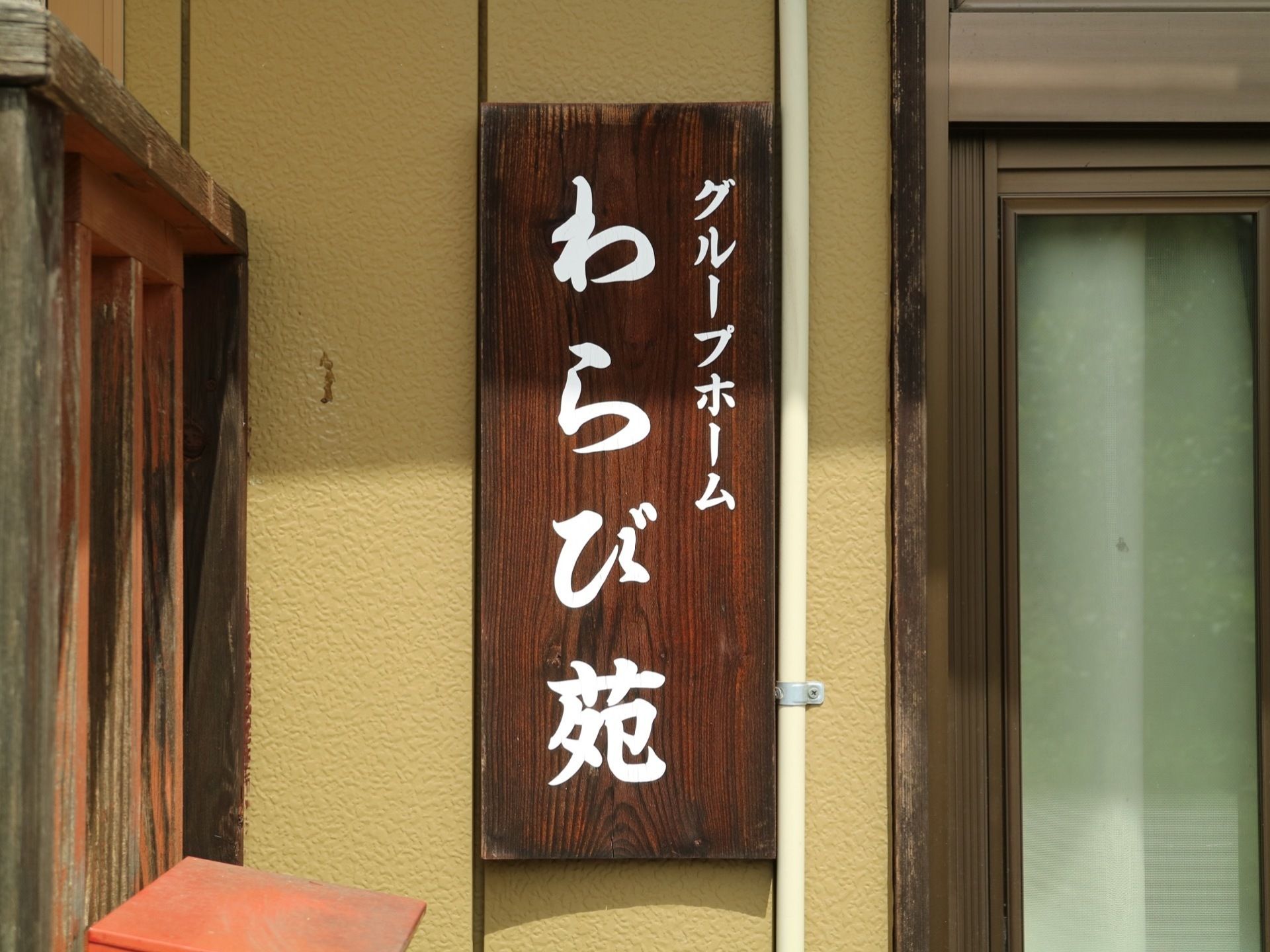 施設入口そばの壁には、施設名のプレートが掲げられている。濃い茶色の木製のプレートで、白い文字で施設の種類と名前が記載されている。