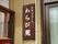 施設の入り口扉の左側に看板が掲示されている。古い板材を小さく切ったものに、白い文字で施設名が書かれている。