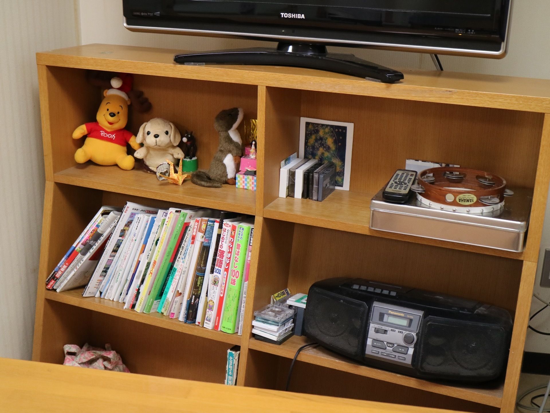 壁際に置かれた木製の棚にたくさんの本が並べられている。ラジカセとカセットテープ、楽器類なども用意されている。