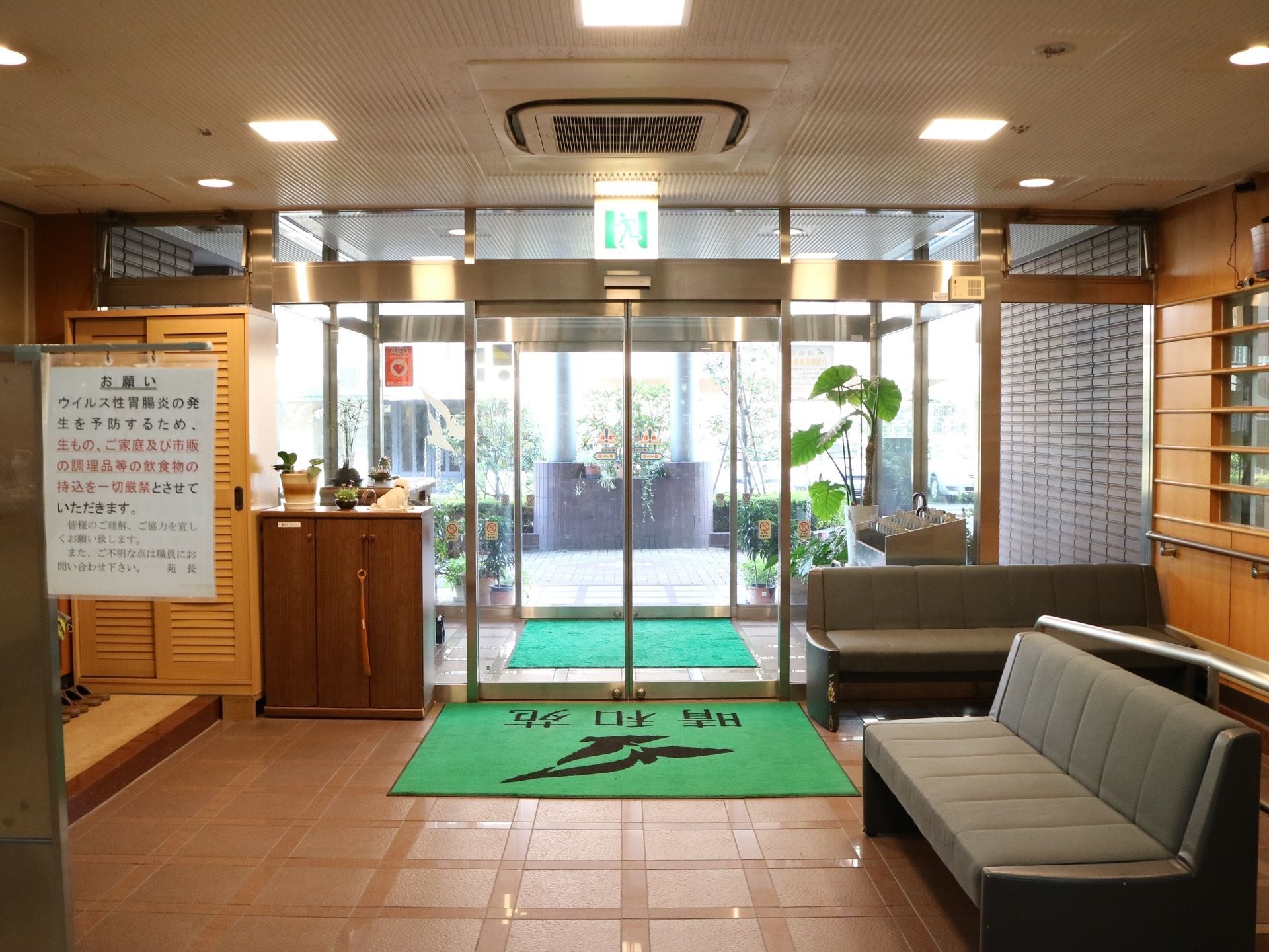 中央奥にガラス扉の入口がある。自動扉になっており、ドアの上にはエアコンが設置されている。床に玄関マットが敷かれている。