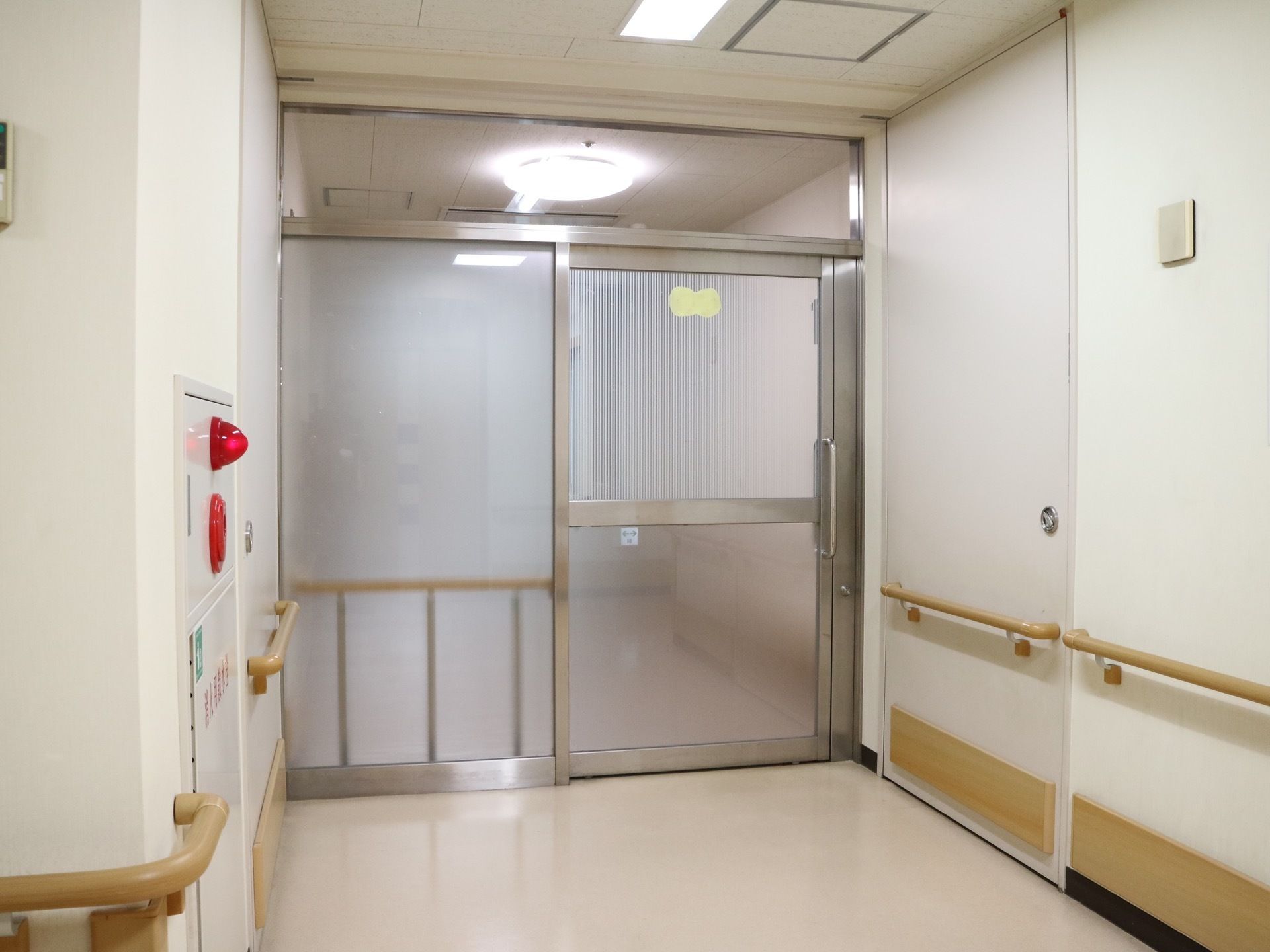 廊下の途中にある区切りの扉はステンレスの自動扉になっている。壁には木製の手すりが取り付けられ、間に防火設備がある。