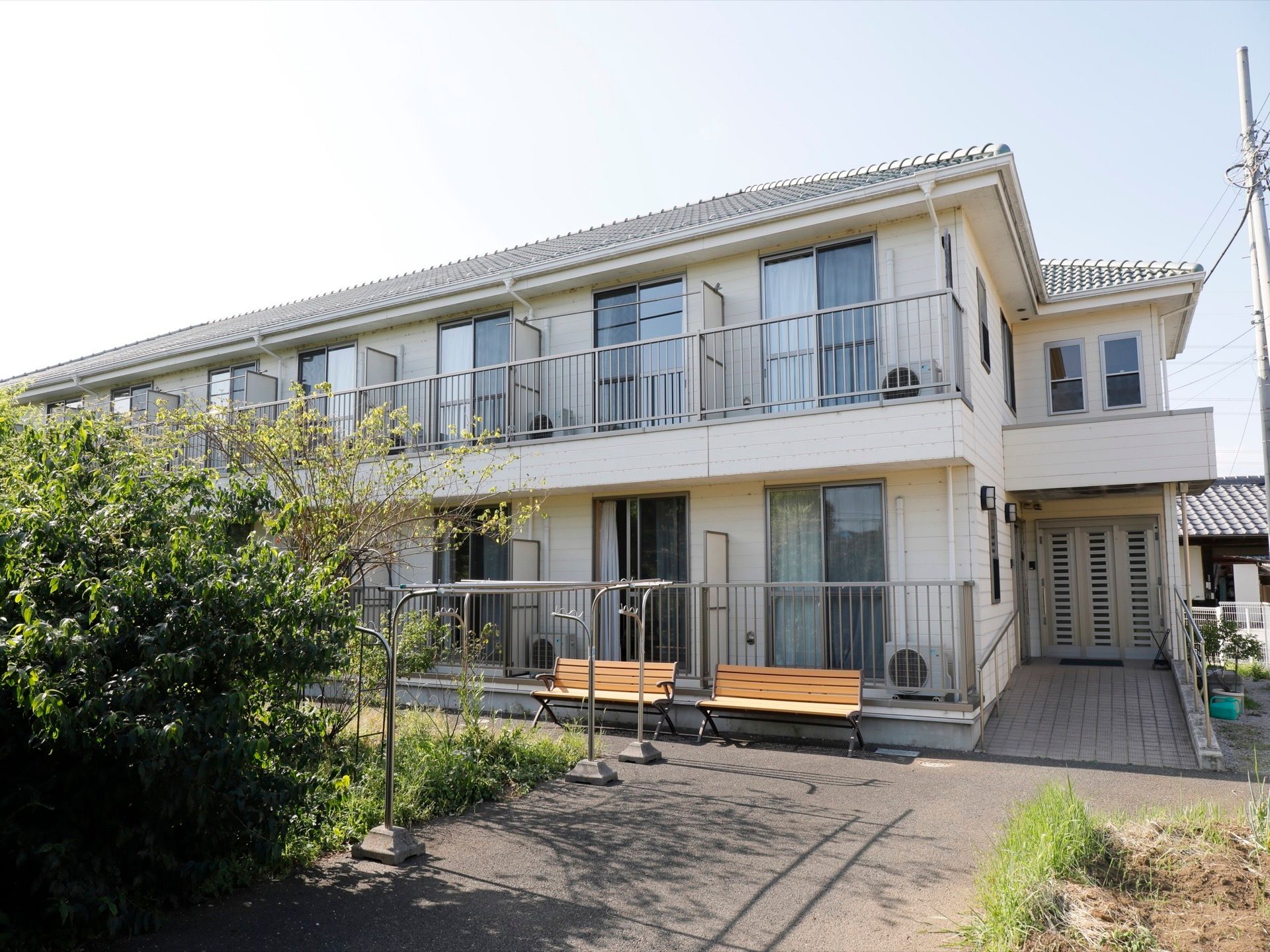 ２階建ての建物で、瓦屋根の一般家屋の佇まいである。施設前にベンチが２脚あり、物干し台が置かれている。