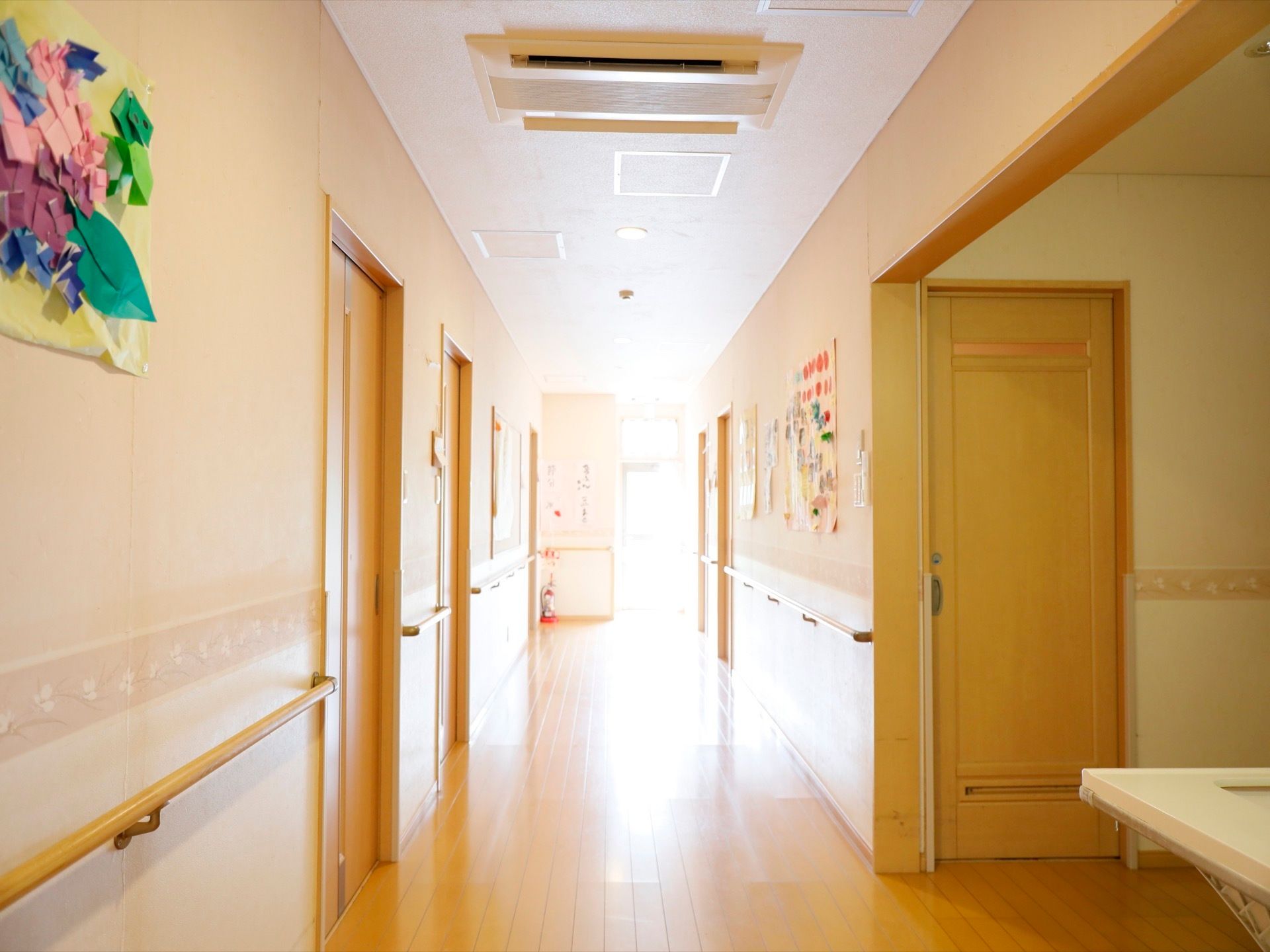 廊下の天井に埋め込み型のエアコンが設置されている。居室のドアが並び、ドア横にネームプレートが取りつけられている。