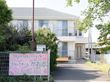 入口の柵に大きな看板が取りつけられており、その上にポストがある。照明が１本立っており、大きな木々が植えられている。
