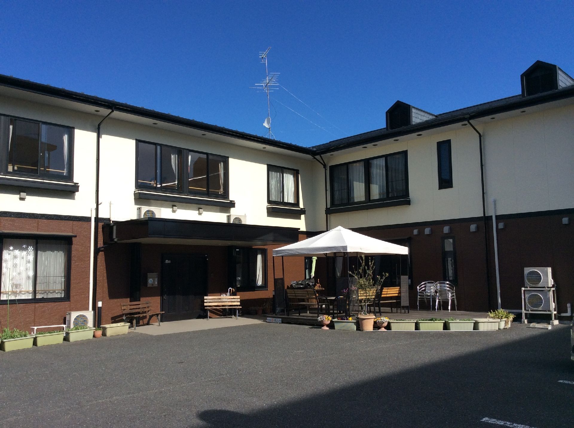 2階建ての建物はフロアにより外壁の色が異なり、敷地内にはパラソル付きのテーブルセットも置かれている。