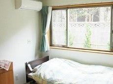 エアコンや窓、ベッドが置かれた居室。ベッドには布団がセットされ、窓にはカーテンが付いている。