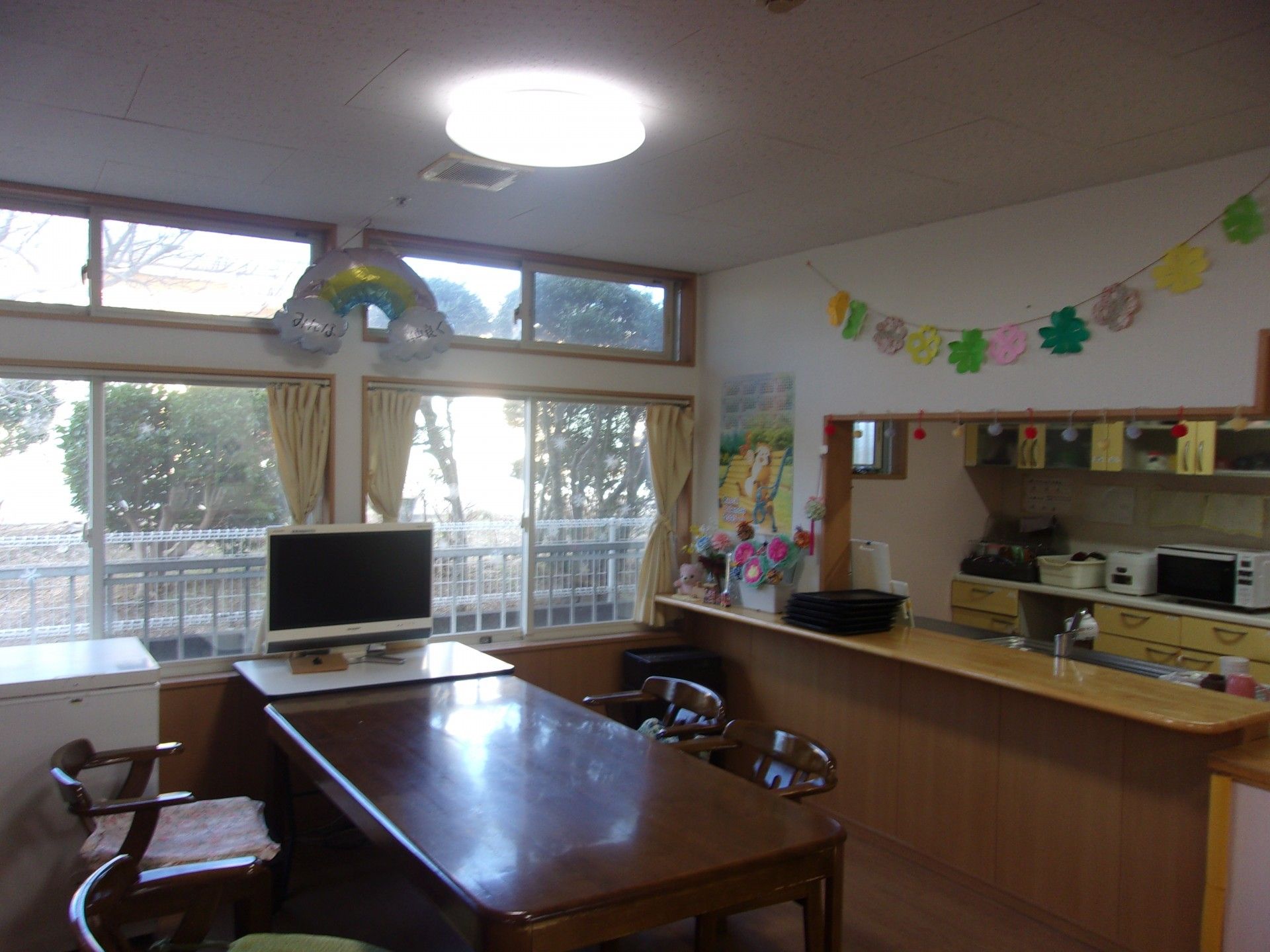 高齢者2名とスタッフが手を握りながら談笑している様子。施設内の会話の一画面