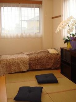 和風にアレンジされた居室。窓にはレースカーテンが設置され、ベッドと収納棚がある。