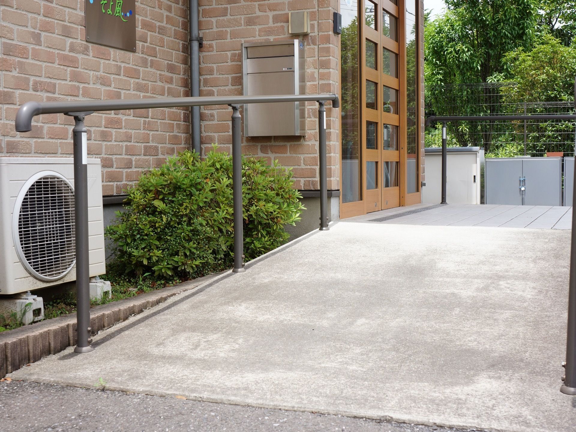 玄関まではスロープを設置しており、補助用の手すりを取り付けている。玄関前の壁にポストが取り付けられている。